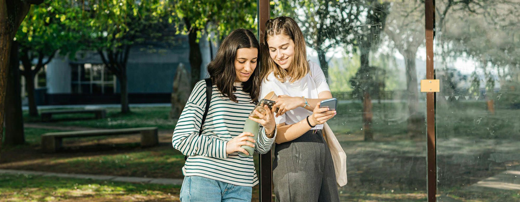 Two women standing next to each other at a bus stop.